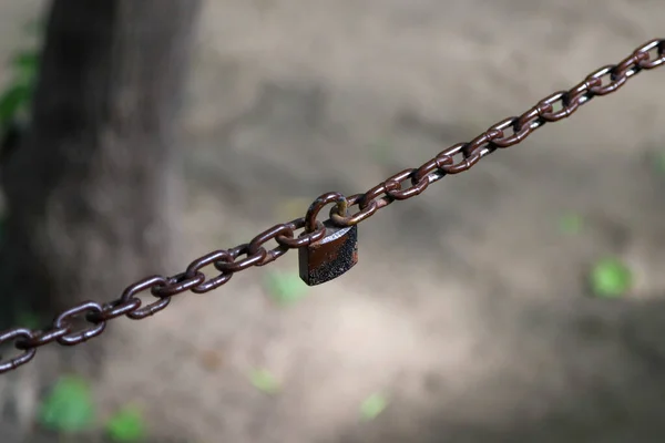 Closeup of a two-parted brown chain connected with an old rusty padlock
