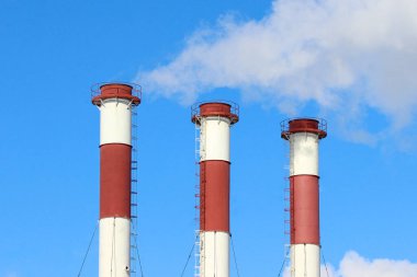 Mavi gökyüzüne karşı sıra sıra dizilmiş üç sanayi bacasından bir duman bulutu.