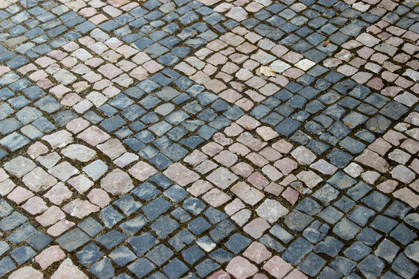 An old stoneblock pavement cobbled with rhombic pattern with small stone blocks of different colors. Photo in perspective