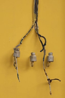 Yeni boyanmış sarı bir duvara el yapımı elektrik hattı monte etmek için üç eski moda seramik yalıtkan.