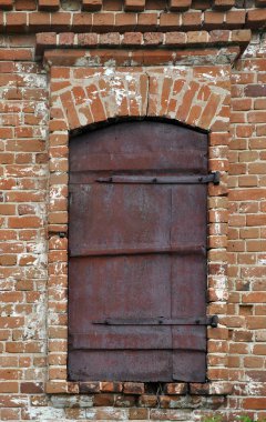 Eski tuğla bir duvarda paslı metal bir pencere perdesi.