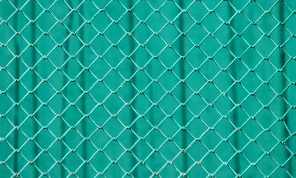 Surface of a wire netting with diamond-shaped elements painted in green in front of a green wall