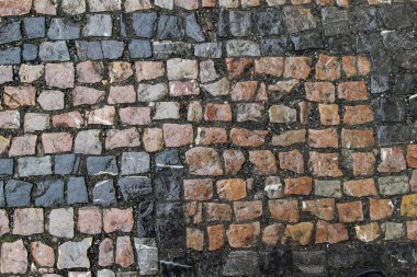 Farklı renklerde taş bloklarla döşenmiş eski hasarlı bir taş kaldırım.