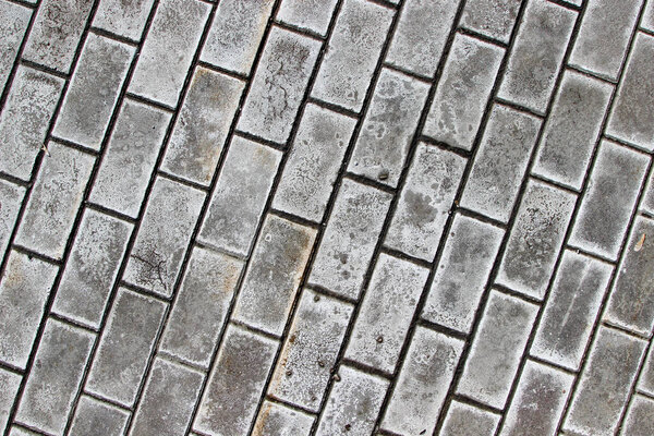 Sidewalk paved with rectangular gray tiles stained with white dirt