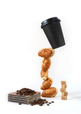 Kağıt kahve fincanı küçük bir kruvasan kulesinde esmer şeker küpleri ve bir parça kağıt üzerinde kahve çekirdekleri ile havaya kaldırılır. Fotoğraf kopyalama alanı olan beyaz üzerine izole edilmiş.