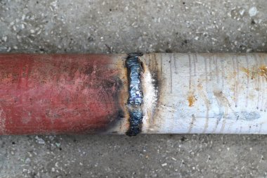 Closeup of a welded butt joint with some defects. Red and white metal pipes welded together