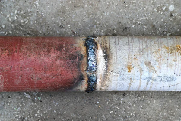 Closeup of a welded butt joint with some defects. Red and white metal pipes welded together