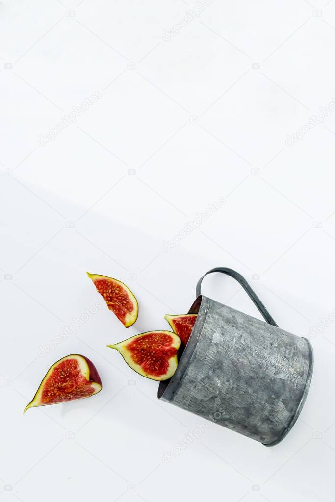 Bright red ripe figs in a metal mug on a white background.