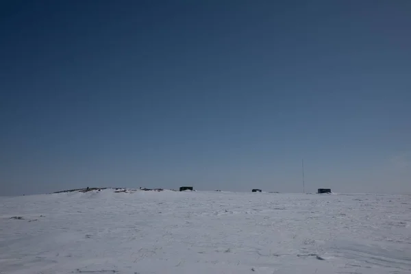 Frozen arctic landscape with snow on the ground with buildings in the background, near Arviat, Nunavut