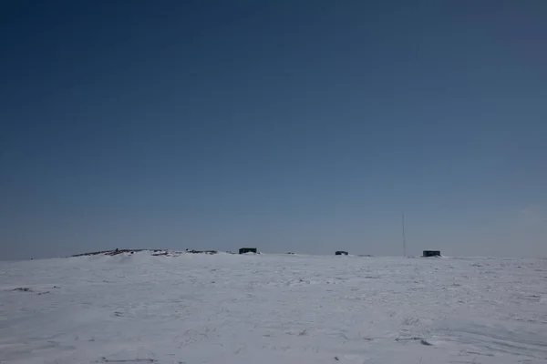 Arviat, Nunavut yakınlarındaki arka planda binalar ve yerde karla kaplı donmuş kutup manzarası.