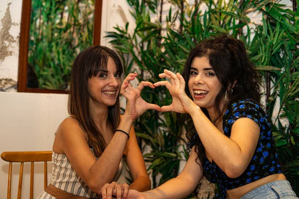 Gülümseyen lezbiyen çift elleriyle doğal yeşil bir arka planda kalp yapıyor.