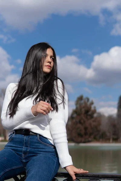 Kot pantolonlu genç bir kız ve arkasında mavi gökyüzü olan beyaz bir kazak.