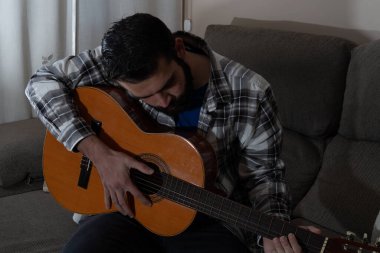 İspanyol gitarı çalan sakallı ve tişörtlü genç adam.