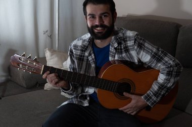 İspanyol gitarı çalan sakallı ve tişörtlü genç adam.