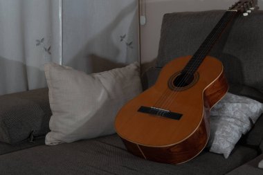 Kahverengi İspanyol gitar seti gri bir kanepede yastıklı.
