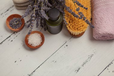 SPA konsepti. Düz katman lavanta çiçekleri, temel yağ, deniz tuzu, düz taşlar, kokulu mum, ahşap arka planda pembe banyo havlusu..