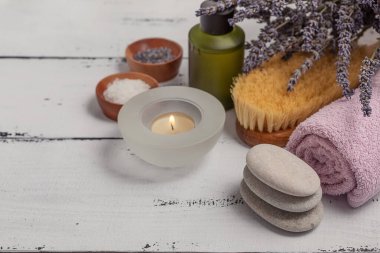 SPA konsepti. Düz katman lavanta çiçekleri, temel yağ, deniz tuzu, düz taşlar, kokulu mum, ahşap arka planda pembe banyo havlusu..