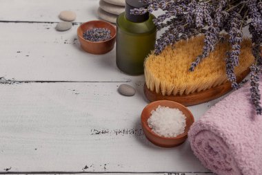 SPA konsepti. Düz katman lavanta çiçekleri, temel yağ, deniz tuzu, düz taşlar, kokulu mum, ahşap arka planda pembe banyo havlusu..