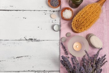 SPA konsepti. Düz katman lavanta çiçekleri, temel yağ, deniz tuzu, düz taşlar, kokulu mum, ahşap arka planda pembe banyo havlusu..