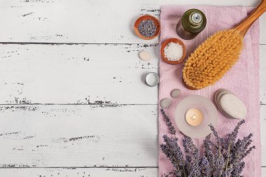 SPA konsepti. Düz katman lavanta çiçekleri, temel yağ, deniz tuzu, düz taşlar, kokulu mum, ahşap arka planda pembe banyo havlusu..