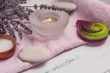 SPA konsepti. Düz katman lavanta çiçekleri, temel yağ, deniz tuzu, düz taşlar, kokulu mum, ahşap arka planda pembe banyo havlusu..