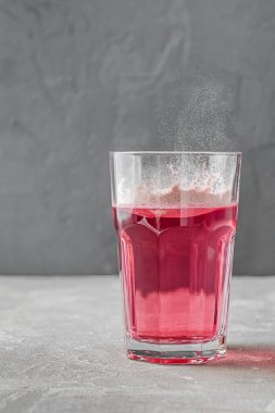 Hidrolize kolajen tozu, pembe renk. Gri arka planda su olan kaşık ve cam bardak. Gıda katkı maddeleri konsepti.