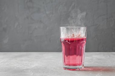 Hidrolize kolajen tozu, pembe renk. Gri arka planda su olan kaşık ve cam bardak. Gıda katkı maddeleri konsepti.