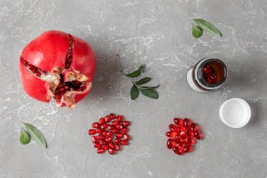 Sağlıklı beslenme, vitamin ve besin takviyeleri kavramının gri arka planında, kapsüllerde yaprakları ve vitaminleri olan kırmızı nar meyveleri.