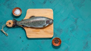 Balık, turkuaz arka planda kesim tahtasındaki baharatlı çiğ alabalık. Boşluğu kopyala