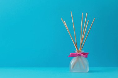 Mavi arka planda ahşap sopaları olan bir cam dağıtıcıda ev kokusu.