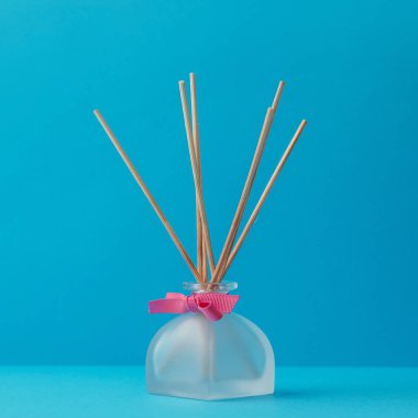 Mavi arka planda ahşap sopaları olan bir cam dağıtıcıda ev kokusu.