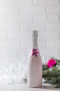 Beyaz bir şişe şampanya, iki boş şarap bardağı ve beyaz tuğlalı bir Noel topu. dikey kare