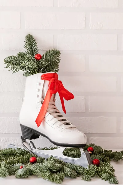 winter composition with figure skates and fir branches on the background of a white brick wall.