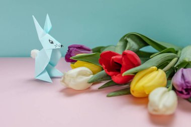 Arka planda renkli bir arka planda bahar laleleri ve origami tavşanı. Paskalya kutlaması, tebrik kartı, bayram davetiyesi. seçici odak