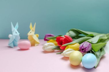 bahar laleleri, pastel renkli Paskalya yumurtaları ve arka planda renkli origami tavşanları. Paskalya kutlaması, tebrik kartı, bayram davetiyesi. seçici odak