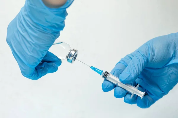 a syringe and a bottle of vaccination in the hands of a woman in blue medical gloves on the background of a light wall. the principle of collective immunity from covid19