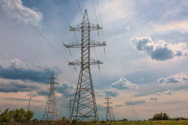 Yüksek voltajlı elektrik hatlarının kutupları, bulutlu gökyüzüne karşı perspektif olarak geriliyor.