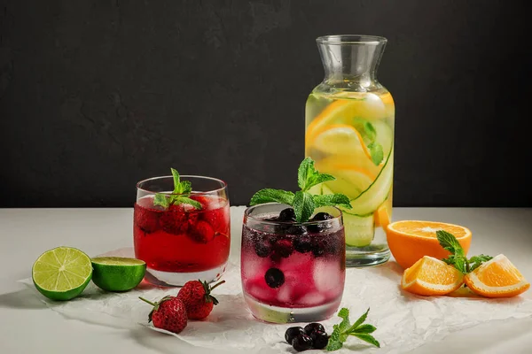 stock image a mix of cold homemade lemonades, in glass glasses and a bottle, mint leaves, citrus slices and berries on a dark background