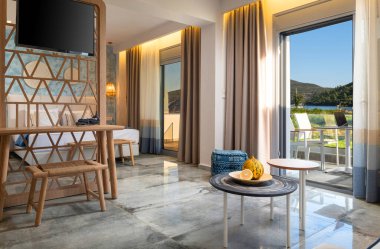 El yapımı hasır ahşap mobilyaları, el yapımı TV bölme ahşap duvarı, açık Fransız pencere terasında yaz manzarası manzarası olan modern çağdaş yatak odası.