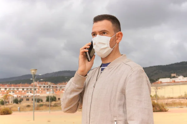 Man wearing reusable facial mask is using a smartphone in an urban background. Reusable masks are an ecological alternative to single use respirators, such as KN95, FFP2, or surgical masks.