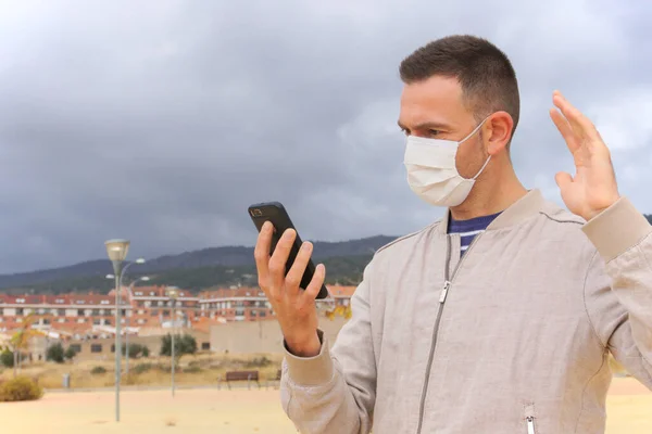 Yeniden kullanılabilir yüz maskesi takan bir adam, arka planda akıllı telefon kullanıyor. Yeniden kullanılabilir maskeler, KN95, FFP2 veya cerrahi maskeler gibi tek kullanımlık solunum cihazlarına ekolojik bir alternatiftir..