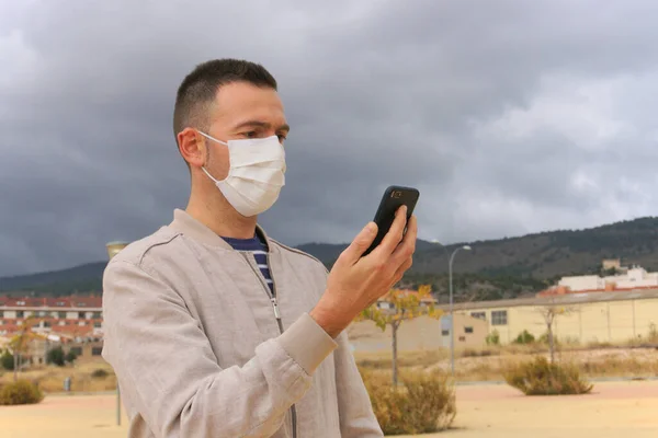 Man wearing reusable facial mask is using a smartphone in an urban background. Reusable masks are an ecological alternative to single use respirators, such as KN95, FFP2, or surgical masks.