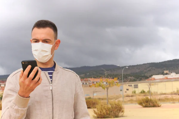 Yeniden kullanılabilir yüz maskesi takan bir adam, arka planda akıllı telefon kullanıyor. Yeniden kullanılabilir maskeler, KN95, FFP2 veya cerrahi maskeler gibi tek kullanımlık solunum cihazlarına ekolojik bir alternatiftir..
