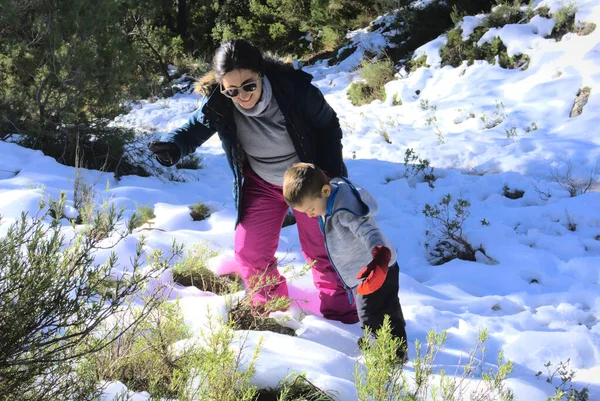 Anne çocuğun kar tepesine tırmanmasına yardım ediyor.