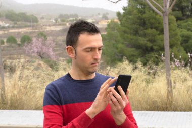 Akıllı telefon kullanan genç bir erkek endişeli bir şekilde ekranı izliyor. Kavram: İletişim