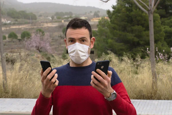 Kameraya bakarak iki akıllı telefon kullanan genç adam şok oldu. Kavram: Sosyal medya bağımlılığı.