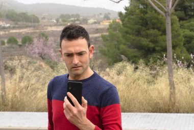 Akıllı telefon kullanan genç bir erkek endişeli bir şekilde ekranı izliyor. Kavram: İletişim