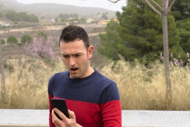 Akıllı telefon kullanan genç bir erkek endişeli bir şekilde ekranı izliyor. Kavram: İletişim