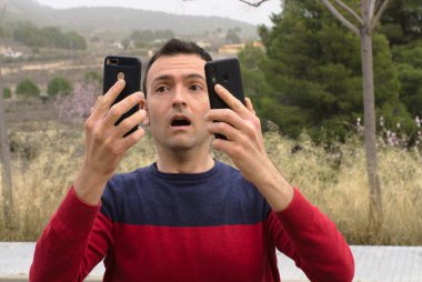 Stresli orta yaşlı adam aynı anda iki cep telefonu kullanıyor. İşkolik kavramı.