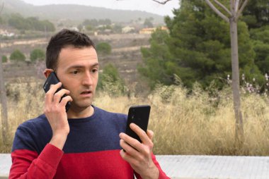 Genç adam ekranda iki akıllı telefon kullanarak şok oldu. Kavram: Sosyal medya bağımlılığı.